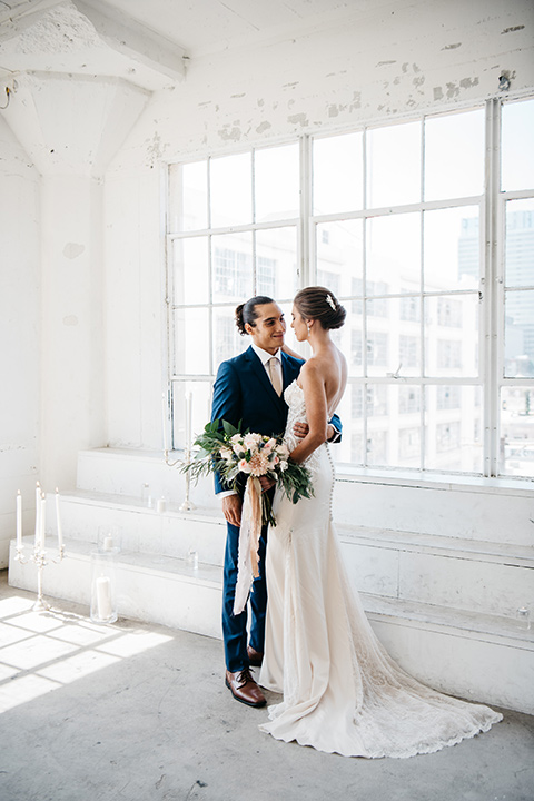 FD-Studios-bridal-gown-from-behind-bride-wearing-a-flowing-strapless-gown-with-a-lace-bodice-groom-in-a-dark-blue-suit-with-a-blush-long-tie