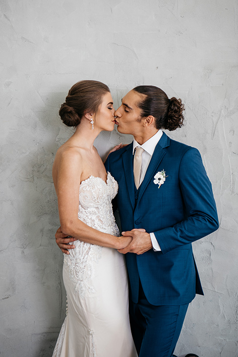 FD-Studios-bride-and-groom-close-by-grey-wall-bride-wearing-a-flowing-strapless-gown-with-a-lace-bodice-groom-in-a-dark-blue-suit-with-a-blush-long-tie