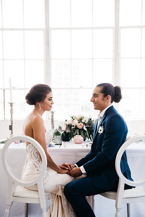 FD-Studios-bride-and-groom-sitting-at-table-bride-wearing-a-flowing-strapless-gown-with-a-lace-bodice-groom-in-a-dark-blue-suit-with-a-blush-long-tie