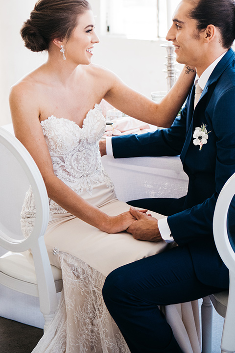 FD-Studios-bride-and-groom-sitting-bride-wearing-a-flowing-strapless-gown-with-a-lace-bodice-groom-in-a-dark-blue-suit-with-a-blush-long-tie