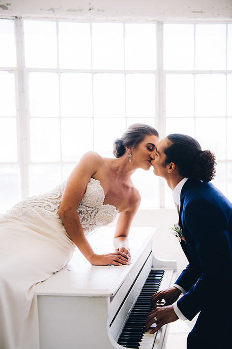 FD-Studios-kissing-on-the-paino-bride-wearing-a-flowing-strapless-gown-with-a-lace-bodice-groom-in-a-dark-blue-suit-with-a-blush-long-tie