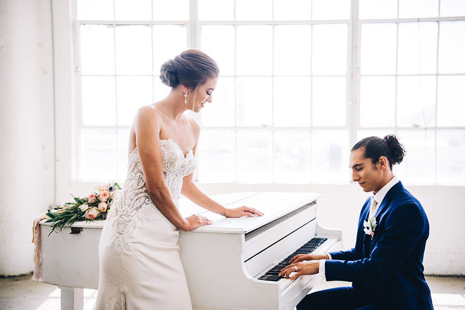 FD-Studios-playing-the-piano-bride-in-a-strapless-flowing-gown-groom-in-a-dark-blue-suit-with-a-blush-long-tie