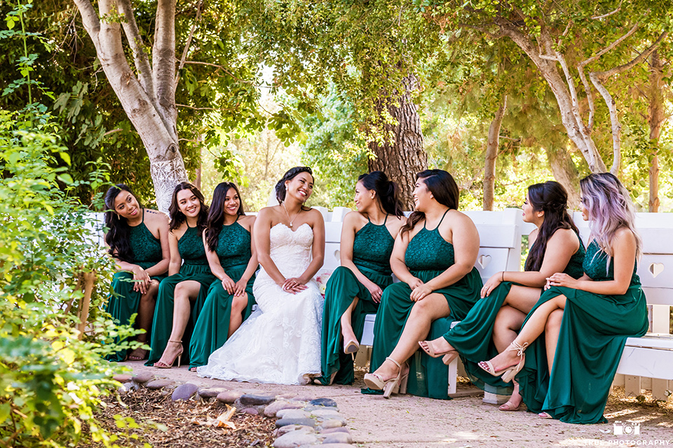 Real-wedding-lani-and-ryan-bridemaids-sitting-on-benches-looking-at-bride-bridesmaids-are-in-dark-green-dresses-with-lace-detailing-and-halter-nekline-bride-in-a-lace-a-line-dress-with-hair-in-a-bun-and-long-veil