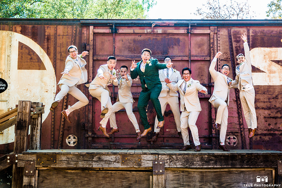 Real-wedding-lani-and-ryan-groomsmen-jumping-by-train-car-groomsmen-in-tan-suits-with-floral-ties-and-brown-shoes-groom-in-green-suit-with-a-floral-tie-and-brown-shoes