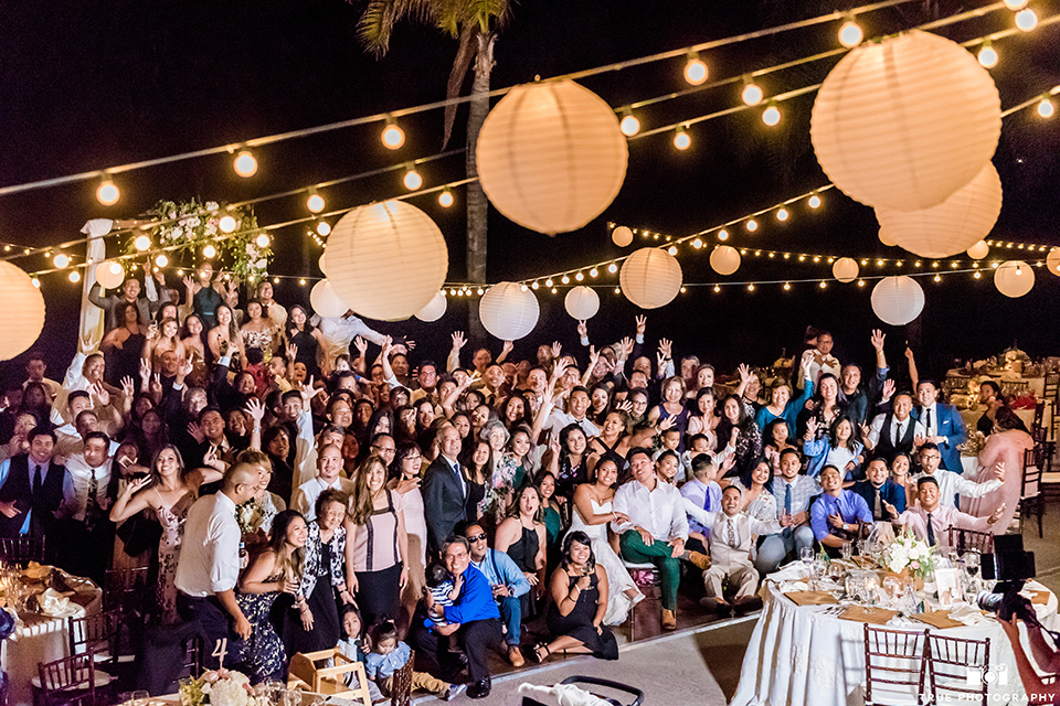 Real-wedding-lani-and-ryan-huge-wedding-picture-with-all-guests-groomsmen-in-tan-suits-with-floral-ties-and-brown-shoes-groom-in-green-suit-with-a-floral-tie-and-brown-shoes-bridesmaids-are-in-dark-green-dresses-with-lace-detailing-and-halter-nekline-bride-in-a-lace-a-line-dress-with-hair-in-a-bun-and-long-veil