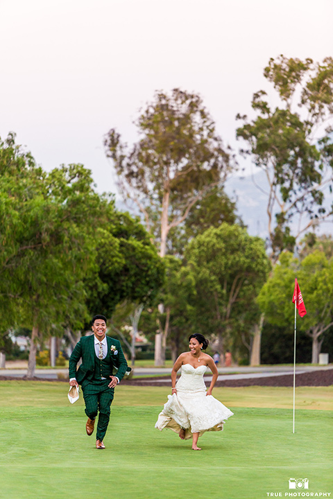 Real-wedding-lani-and-ryan-running-on-the-gold-course-groom-in-green-suit-with-a-floral-tie-and-brown-shoes-bride-in-a-lace-a-line-dress-with-hair-in-a-bun-and-long-veil