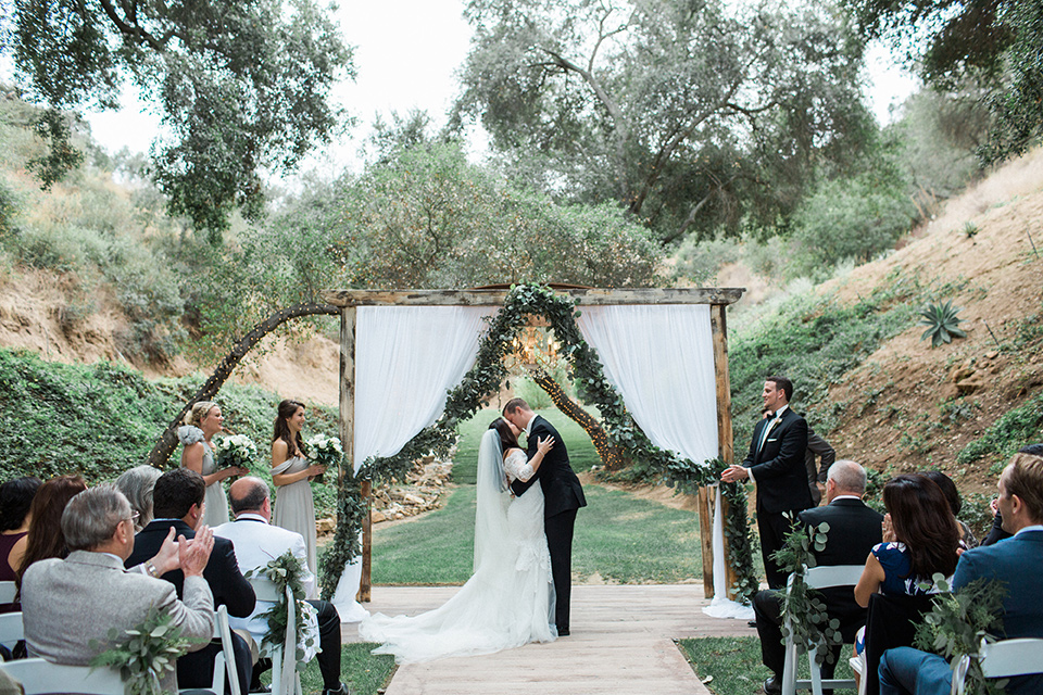 los-willows-wedding-ceremony-firsr-kiss-bride-in-a-tulle-ballgown-with-sleeves-groom-in-a-traditional-black-tuxedo-with-black-bow-tie-and-tuxed-shoes