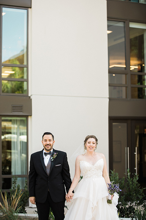 Avenue-of-the-arts-wedding-bride-and-groom-facing-camera-in-front-of-building-bride-in-tulle-ball-gown-with-beaded-bodice-and-beaded-headband-groom-inblack-tuxedo-with-a-silver-vest-and-silver-bowtie