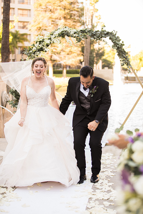 Avenue-of-the-arts-wedding-bride-and-groom-jumping-one-bride-in-tulle-ball-gown-with-beaded-bodice-and-beaded-headband-groom-inblack-tuxedo-with-a-silver-vest-and-silver-bowtie