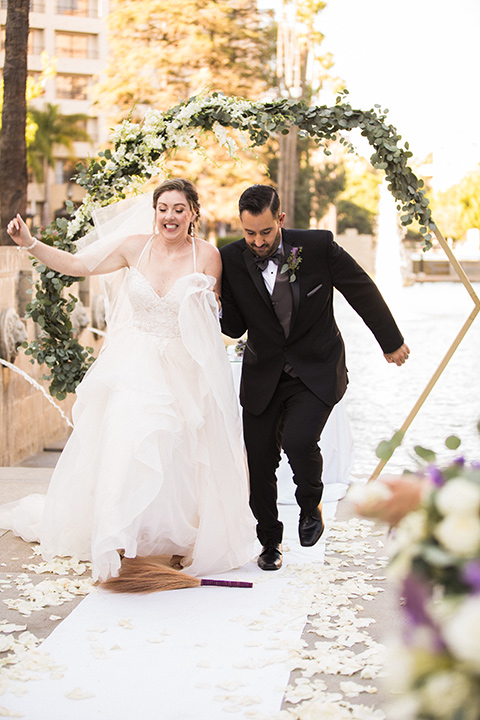 Avenue-of-the-arts-wedding-bride-and-groom-jumping-two-bride-in-tulle-ball-gown-with-beaded-bodice-and-beaded-headband-groom-inblack-tuxedo-with-a-silver-vest-and-silver-bowtie