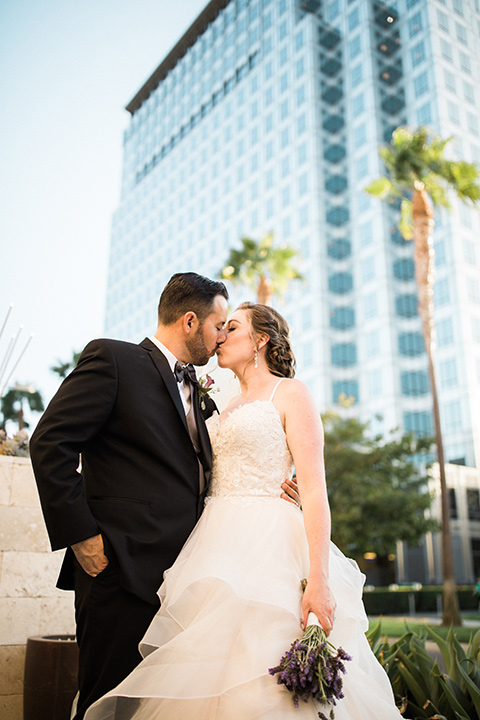 Avenue-of-the-arts-wedding-bride-and-groom-with-tall-buildings-behind-the-bride-in-tulle-ball-gown-with-beaded-bodice-and-beaded-headband-groom-inblack-tuxedo-with-a-silver-vest-and-silver-bowtie