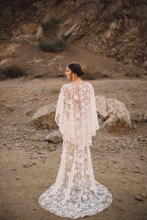 bronson-caves-elopement-shoot-bride-from-behind-bride-wearing-a-lace-boho-inspired-dresswith-a-flowing-cape-detail-and-hair-up-in-a-mess-braided-bun
