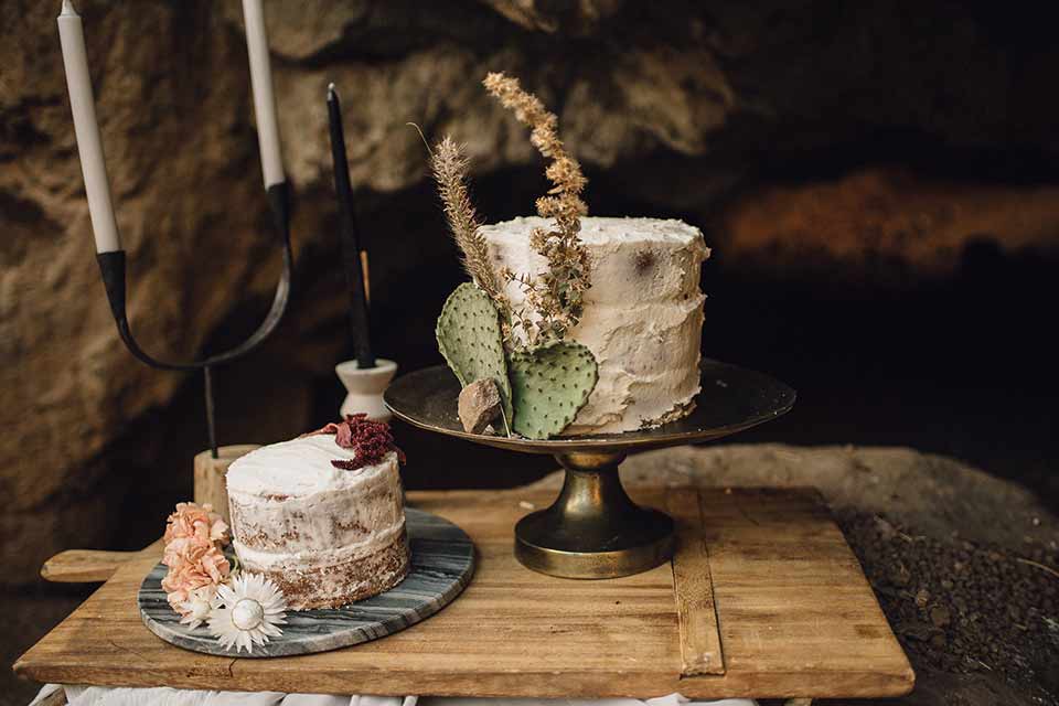 bronson-caves-elopement-shoot-cake-bride-wearing-a-lace-boho-inspired-dresswith-a-flowing-cape-detail-and-hair-up-in-a-mess-braided-bun-the-groom-wore-a-navy-suit-with-a-silver-tie