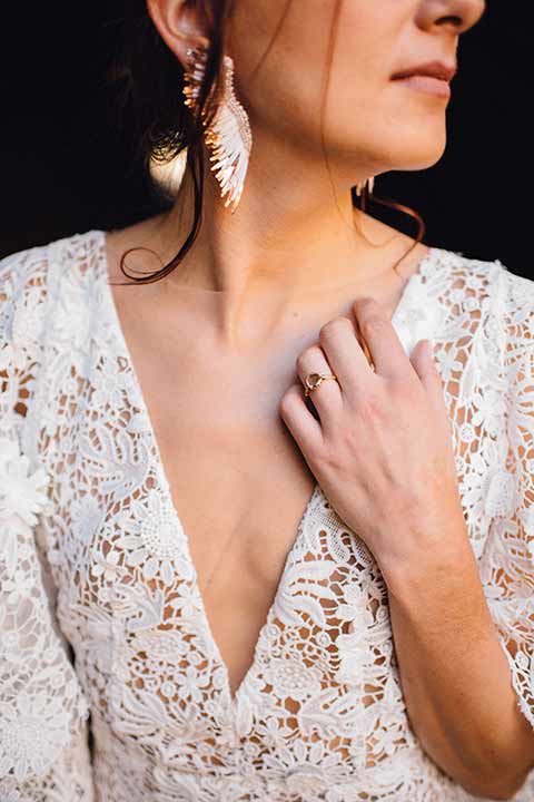 bronson-caves-elopement-shoot-close-up-of-bridal-jewelry-bride-wearing-a-lace-boho-inspired-dresswith-a-flowing-cape-detail-and-hair-up-in-a-mess-braided-bun