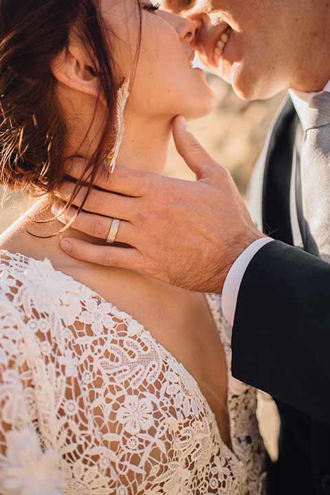 bronson-caves-elopement-shoot-close-up-of-bride-and-groom-kissing-bride-wearing-a-lace-boho-inspired-dresswith-a-flowing-cape-detail-and-hair-up-in-a-mess-braided-bun-the-groom-wore-a-navy-suit-with-a-silver-tie