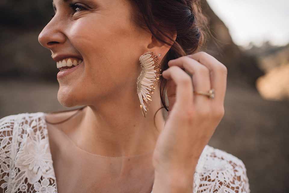 bronson-caves-elopement-shoot-close-up-on-bride-bride-wearing-a-lace-boho-inspired-dresswith-a-flowing-cape-detail-and-hair-up-in-a-mess-braided-bun