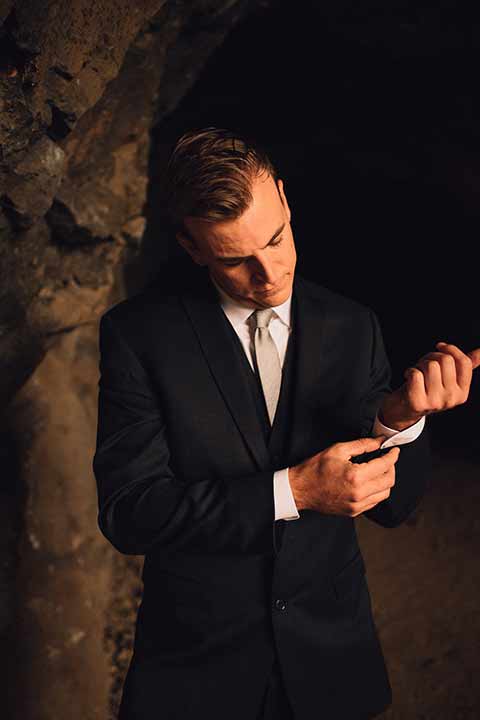 bronson-caves-elopement-shoot-groom-fixing-cuff-groom-in-cave-groom-wore-a-navy-suit-with-a-silver-tie