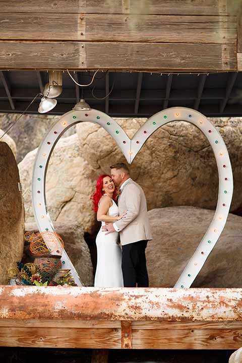 Desert-view-tower-bride-and-groom-recetiption-laughing-bride-in-a-fitted-satin-dress-with-a-high-neckline-and-hot-pink-hair-groom-in-a-tan-coat-with-black-pants-and-a-blue-tie