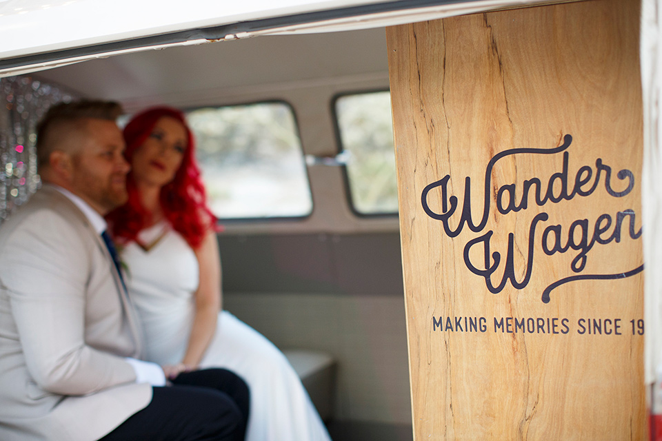 Desert-view-tower-bride-and-groom-wander-wagon-bride-in-a-fitted-satin-dress-with-a-high-neckline-and-hot-pink-hair-groom-in-a-tan-coat-with-black-pants-and-a-blue-tie