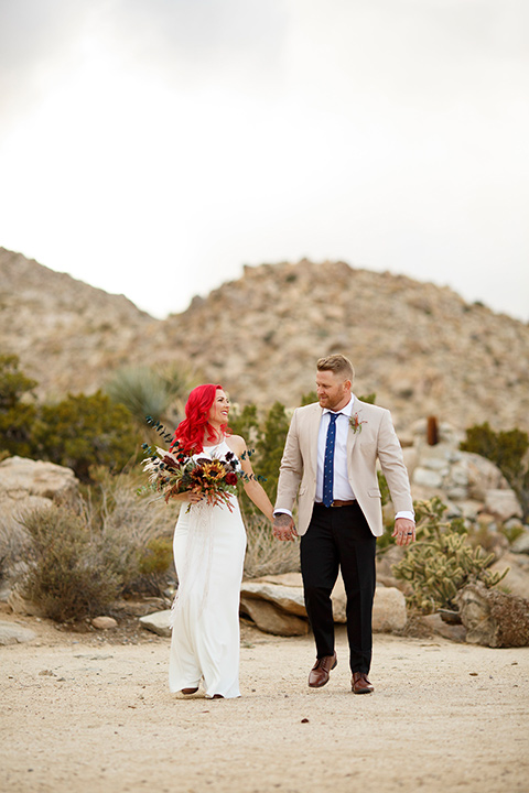 Desert-view-tower-bride-and-groom-holding-hands-bride-in-a-fitted-satin-dress-with-a-high-neckline-and-hot-pink-hair-groom-in-a-tan-coat-with-black-pants-and-a-blue-tie