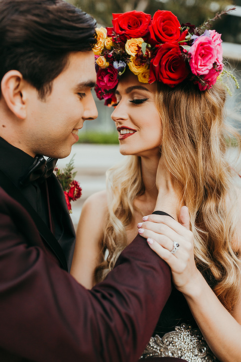 dia-de-los-muertos-color-background-bride-wearing-a-black-dress-and-floral-headpeice-groom-wearing-a-burgundy-tux-with-black-tri-and-black-shirt-with-black-bow-tie