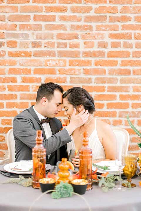 estate-on-second-shoot-bride-and-groom-heads-touching-bride-wearing-a-flowing-white-gown-with-thin-straps-and-hair-in-a-messy-boho-french-braid-groom-in-a-charcoal-grey-tuxedo-with-a-dark-brown-bow-and-shoes