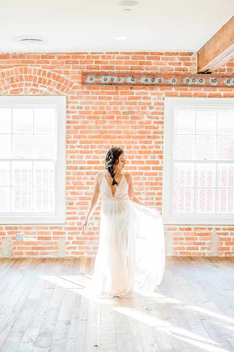 estate-on-second-shoot-bride-near-bricks-bride-wearing-a-flowing-white-gown-with-thin-straps-and-hair-in-a-messy-boho-french-braid 