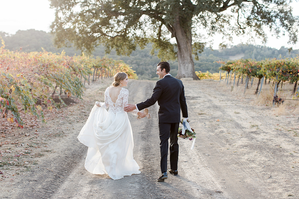 hammersky-editorial-shoot-bride-and-groom-walking-away-from-camera-bride-in-a-tulle-ballgown-with-lace-sleeves-and-high-neckline-groom-in-a-black-shawl-lapel-tuxedo-with-black-bow