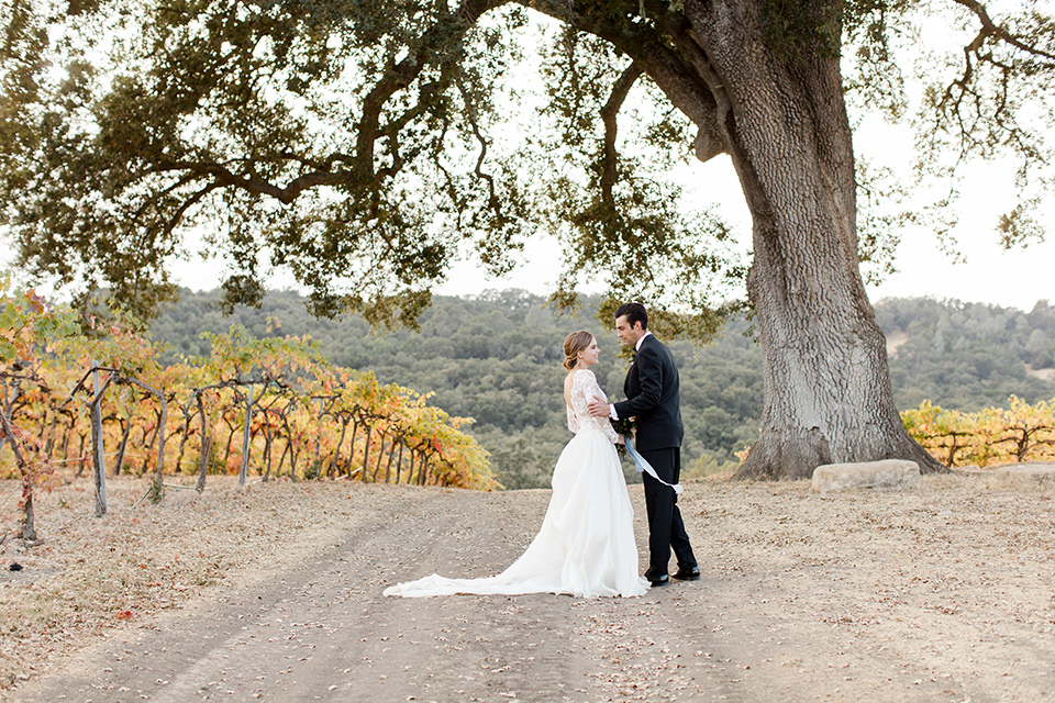 hammersky-editorial-shoot-bride-and-groom-walking-together-on-path-bride-in-a-tulle-ballgown-with-lace-sleeves-and-high-neckline-groom-in-a-black-shawl-lapel-tuxedo-with-black-bow