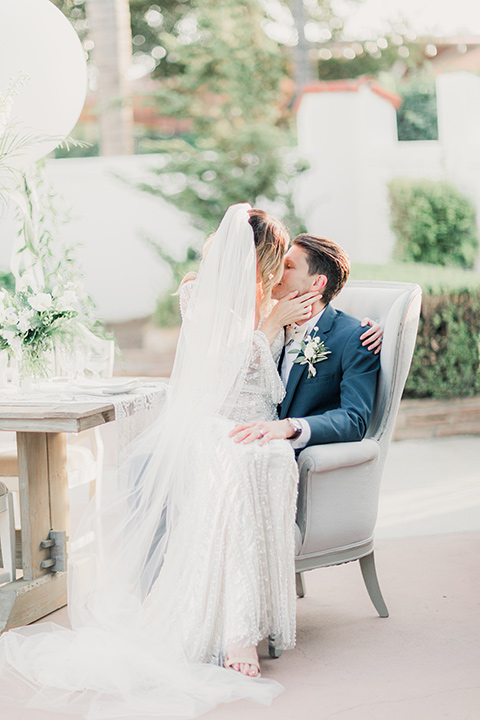 MUCKENTHALER-SHOOT-bride-and-groom-sitting-in-chair-bride-in-fitted-satin-long-sleeve-gown-groom-in-a-slate-blue-suit-with-a-ivory-bow-tie