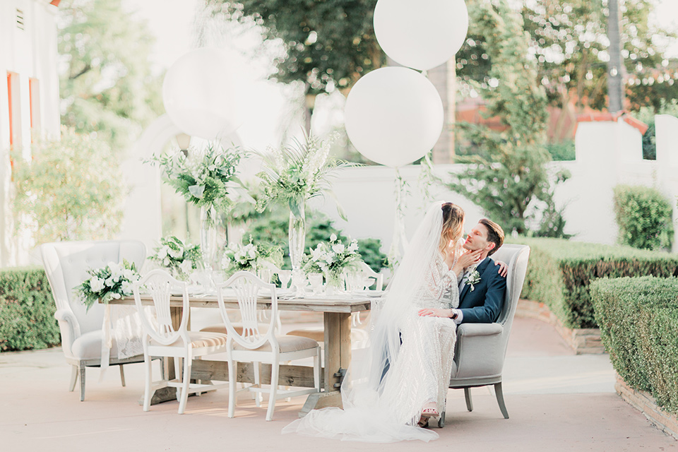 MUCKENTHALER-SHOOT-bride-sitting-on-groom-on-chair-bride-in-fitted-satin-long-sleeve-gown-groom-in-a-slate-blue-suit-with-a-ivory-bow-tie