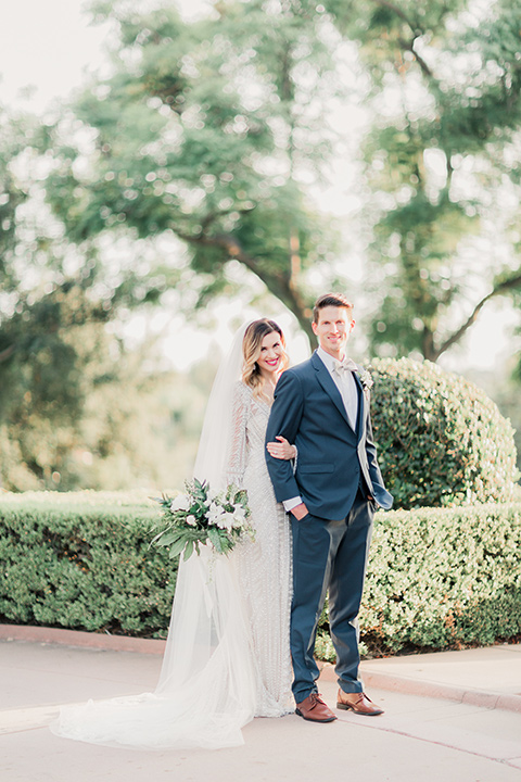 MUCKENTHALER-SHOOT-bride-standing-behind-groom-bride-in-fitted-satin-long-sleeve-gown-groom-in-a-slate-blue-suit-with-a-ivory-bow-tie