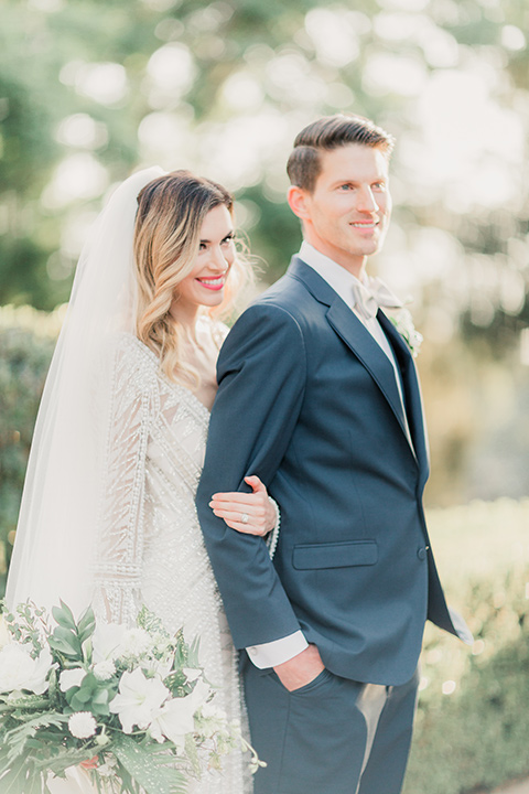 MUCKENTHALER-SHOOT-bride-standing-behind-groom-bride-in-fitted-satin-long-sleeve-gown-groom-in-a-slate-blue-suit-with-a-ivory-bow-tie