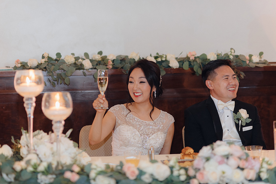 occidental-college-wedding-bride-and-groom-at-sweetheart-table-groom-in-black-tuxedo-bride-in-a-fitted-gown-with-a-beaded-bodice-bridesmaids-in-blue-gowns