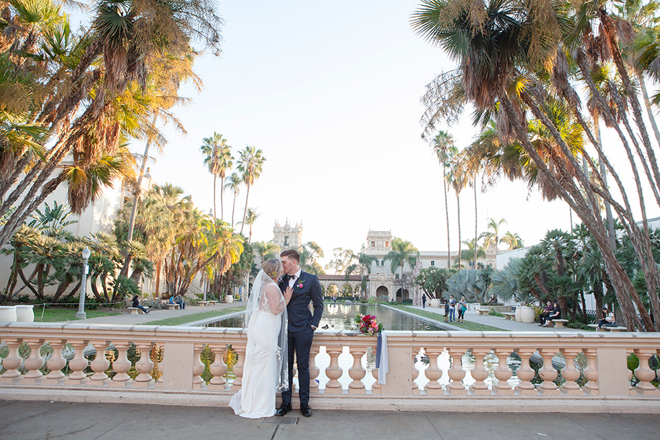 parq-west-shoot-brdide-and-groom-kissing-outside-on-bridge-bride-wearing-a-flowing-gown-with-an-illusion-lace-bodice-and-cap-sleeves-groom-in-a-charcoal-tuxedo-with-a-black-satin-shawl-lapel