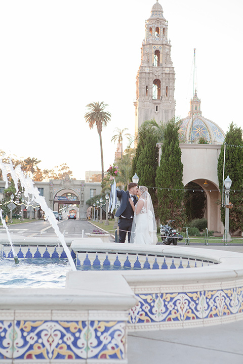 parq-west-shoot-bride-and-groom-by-fountain-bride-wearing-a-flowing-gown-with-an-illusion-lace-bodice-and-cap-sleeves-groom-in-a-charcoal-tuxedo-with-a-black-satin-shawl-lapel