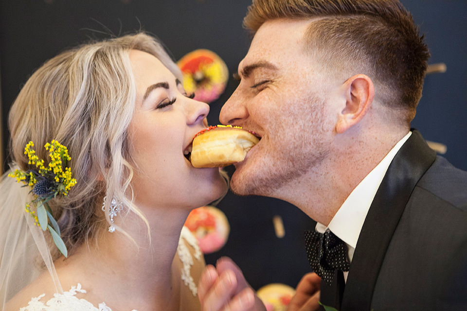 parq-west-shoot-couple-eating-the-donut-bride-wearing-a-flowing-gown-with-an-illusion-lace-bodice-and-cap-sleeves-groom-in-a-charcoal-tuxedo-with-a-black-satin-shawl-lapel