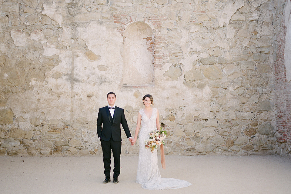 san-juan-capastrano-wedding-bride-and-groom-looking-at-camera-bride-in-a-white-fitted-silk-dress-with-cap-sleeves-and-an-illusion-neckline-and-back-groom-in-a-black-tuxedo-with-black-bow-tie