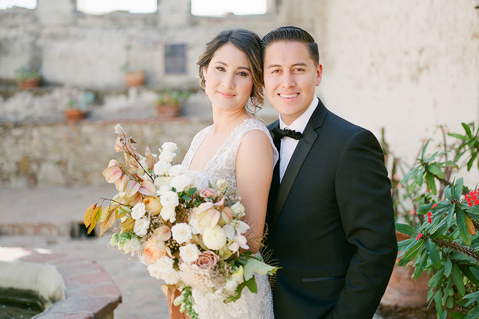 san-juan-capastrano-wedding-bride-and-groom-smiling-bride-in-a-white-fitted-silk-dress-with-cap-sleeves-and-an-illusion-neckline-and-back-groom-in-a-black-tuxedo-with-black-bow-tie