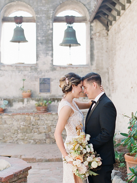 san-juan-capastrano-wedding-bride-and-groom-touching-heads-bride-in-a-white-fitted-silk-dress-with-cap-sleeves-and-an-illusion-neckline-and-back-groom-in-a-black-tuxedo-with-black-bow-tie