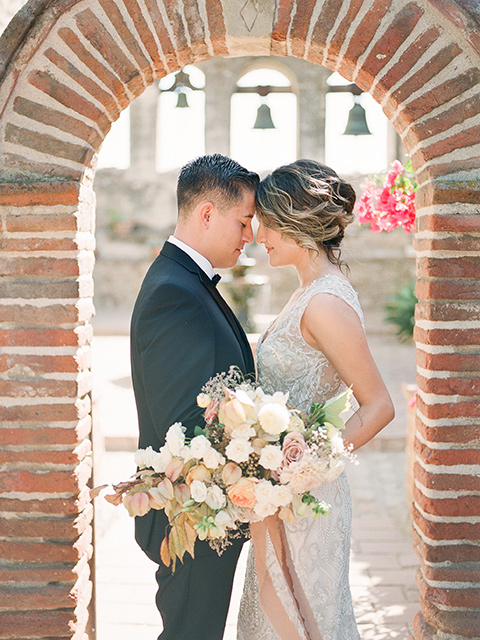 san-juan-capastrano-wedding-close-u-of-bride-and-groom-by-bricks-bride-in-a-white-fitted-silk-dress-with-cap-sleeves-and-an-illusion-neckline-and-back-groom-in-a-black-tuxedo-with-black-bow-tie