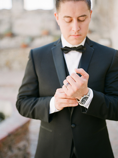 san-juan-capastrano-wedding-close-up-groom-fixing-sleeve-groom-in-a-black-tuxedo-with-black-bow-tie