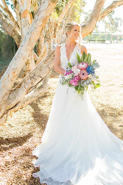 seapoint-bridal-shoot-bride-alone-with-florals-bride-in-a-lace-gown-with-thick-lace-straps-and-hair-in-a-loose-braid