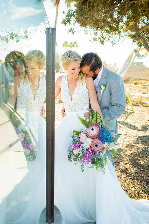 seapoint-bridal-shoot-bride-and-groom-laughing-bride-in-a-lace-gown-with-thick-lace-straps-and-hair-in-a-loose-braid-groom-in-a-light-grey-suit-with-a-white-long-tie