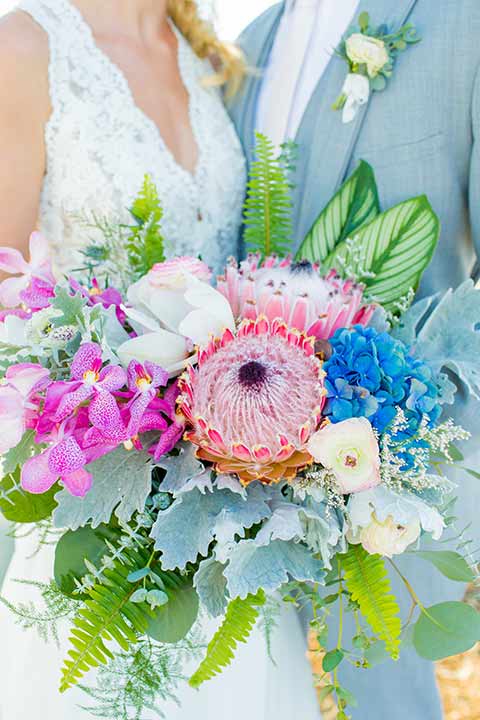 seapoint-bridal-shoot-close-up-on-florals-andbride-and-groom-bride-in-a-lace-gown-with-thick-lace-straps-and-hair-in-a-loose-braid-groom-in-a-light-grey-suit-with-a-white-long-tie