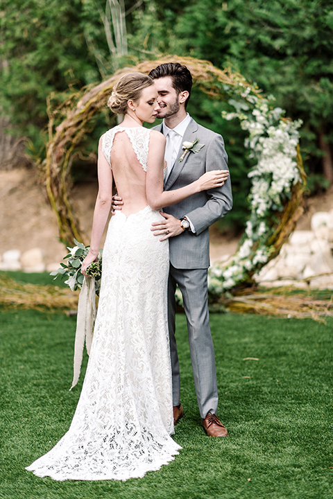 skypark-styled-shoot-bride-and-groom-at-ceremony-space-bride-in-lace-fitted-dress-with-a-sleeves-and-a-keyhole-back-detail-groom-in-grey-suit-with-brown-shoes-and-ivory-long-tie