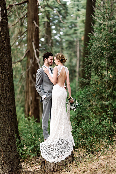 skypark-styled-shoot-bride-and-groom-near-trees-bride-in-lace-fitted-dress-with-a-sleeves-and-a-keyhole-back-detail-groom-in-grey-suit-with-brown-shoes-and-ivory-long-tie