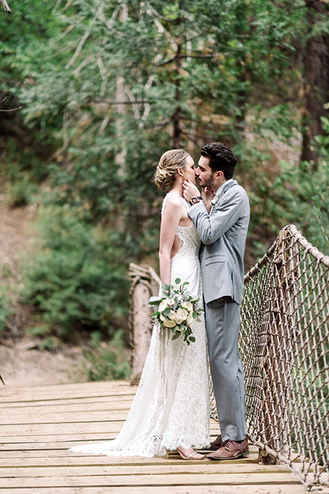 skypark-styled-shoot-bride-and-groom-on-bridge-bride-in-lace-fitted-dress-with-a-sleeves-and-a-keyhole-back-detail-groom-in-grey-suit-with-brown-shoes-and-ivory-long-tie