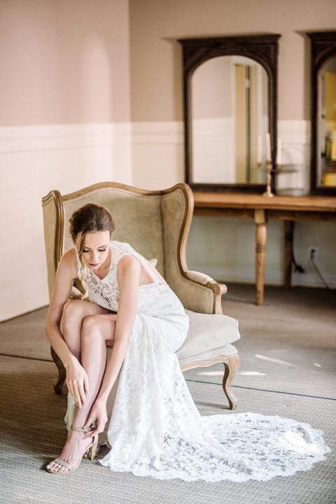 skypark-styled-shoot-bride-putting-on-shoe-bride-in-lace-fitted-dress-with-a-sleeves-and-a-keyhole-back-detail