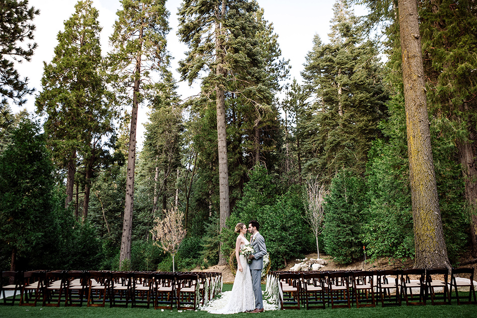 skypark-styled-shoot-long-shot-of-ceremony-space-bride-in-lace-fitted-dress-with-ca-sleeves-and-a-keyhole-back-detail-groom-in-grey-suit-with-brown-shoes-and-ivory-long-tie